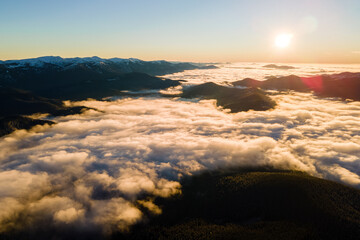 Aerial view of vibrant sunrise over white dense clouds with distant dark mountains on horizon