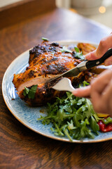 Knife cutting into roasted chicken breast on a blue plate with salad greens and potatoes