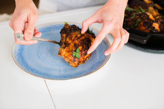 Closeup Of Woman Putting A Piece Of Roast Chicken On A Blue Plate