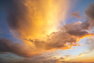 Dramatic yellow sunset landscape with puffy clouds lit by orange setting sun and blue sky