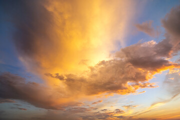 Dramatic yellow sunset landscape with puffy clouds lit by orange setting sun and blue sky