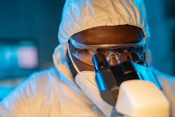Close-up of young African American scientist in protective coveralls, respirator and eyeglasses...