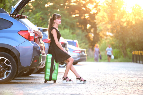 Young woman with suitcase bag waiting beside car. Travelling and vacations concept