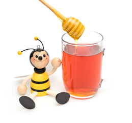 Smiley bee toy next to a glass of fresh juice with a honey stick isolated on a white background