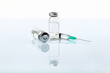 Glass vials with clear liquid next to a syringe and hypodermic needle on a medical table.