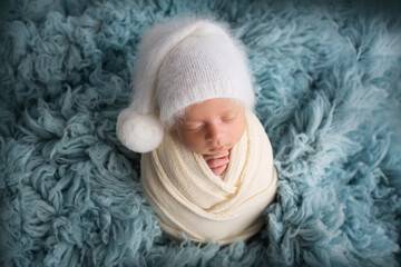Sleeping newborn baby boy in the first days of life in a white soft cocoon with a knitted woolen...
