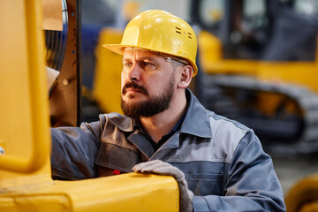 Serious foreman or repairman in boilersuit and safety helmet checking motor of huge industrial...