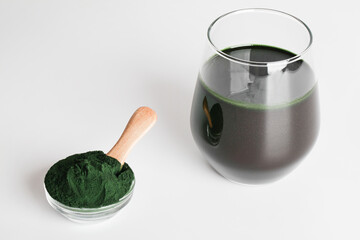 fresh green drink with spirulina in glass, spirulina powder with spoon on white background. useful habits, self care and healthy lifestyle.copy space