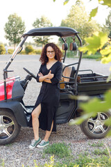 Fototapeta na wymiar Young beautiful curly woman with curly hair in black dress, poses near vehicle and smiling.