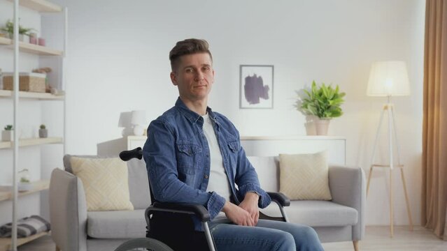 Indoors portrait of serene middle aged man with disability sitting at wheelchair and looking at camera at home