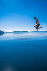 Adventurous athletic man jumping off a pier into a body of calm water.