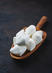 Traditionelle afghanische getrocknete Quark Kaschk Stücke auf einer kleinen Holzschaufel als close-up auf schwarzem rustikalem Hintergrund mit Textfreiraum