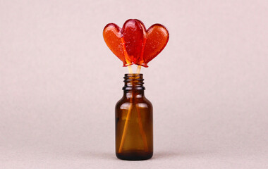 Two red heart-shaped lollipops in a small glass bottle on a gray background