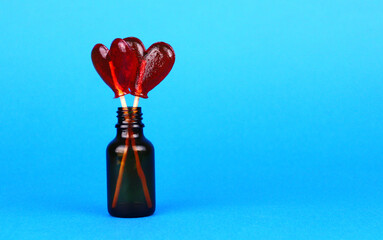 Two red lollipops in shape of a heart in a small glass bottle on a blue background