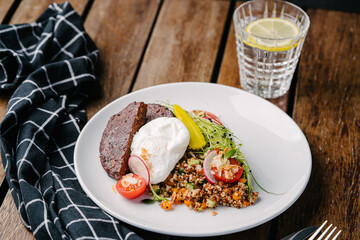Bowl with quinoa, vegetable meat, patzot egg. avocado, carrot, cucumber, cherry tomato, pickled corn, radish, microgreen. On a wooden table. Copy space