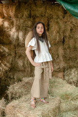 Preteen brunette girl posing on haystack in hayloft in summer country estate