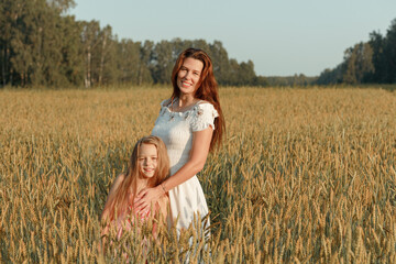 Little girl kisses, hugs a young woman in spikelets of rye.