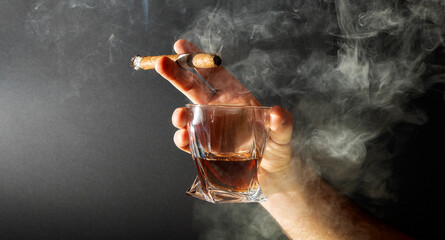 Whiskey and cigar in hand isolated on black background. A glass of whiskey or cognac with a Smoking...