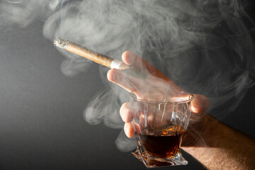 Whiskey and cigar in hand isolated on black background. A glass of whiskey or cognac with a Smoking...