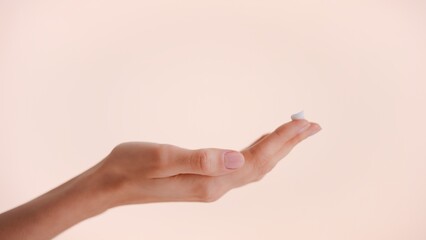 Close-up shot of a female hand with a drop of skin care cream on the top of her finger against nude background