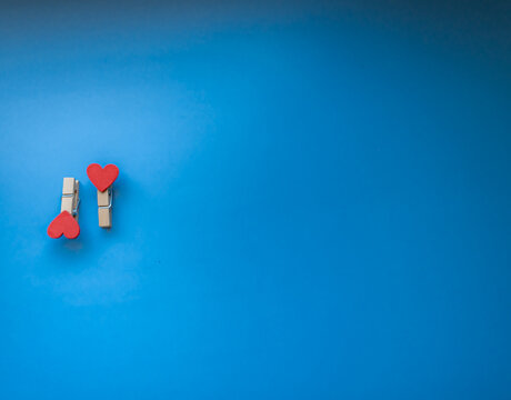 two heart-shaped wooden clothespins lie to right on bright blue background. free place