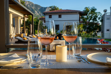 Wine and wine glasses, forks, knives, plates on a table in hotel poolside restaurant served for dinner.