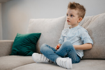 Happy boy playing video games holding game controller sitting on the coach in living room