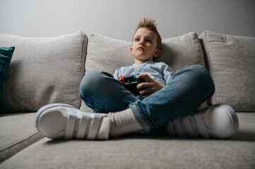 Happy boy playing video games holding game controller sitting on the coach in living room