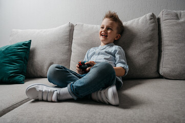 Happy boy playing video games holding game controller sitting on the coach in living room