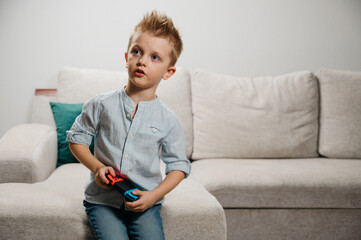 Happy boy playing video games holding game controller sitting on the coach in living room