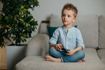 Happy boy playing video games holding game controller sitting on the coach in living room