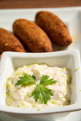 Vegan food, vegan kibbeh and sauce on a white plate, over wood, selective focus.