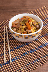 Vegan food, Vegan Yakisoba, with chopsticks in a bowl on bamboo mat, over wood, selective focus.