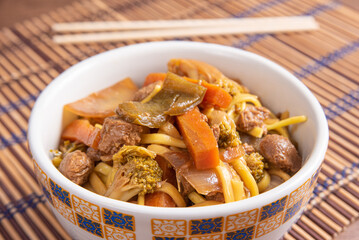 Vegan food, Vegan Yakisoba, with chopsticks in a bowl on bamboo mat, over wood, selective focus.