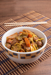 Vegan food, Vegan Yakisoba, with chopsticks in a bowl on bamboo mat, over wood, selective focus.