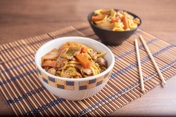 Vegan food, Vegan Yakisoba, with chopsticks in a bowl on bamboo mat, over wood, selective focus.