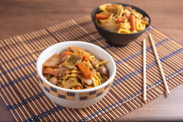 Vegan food, Vegan Yakisoba, with chopsticks in a bowl on bamboo mat, over wood, selective focus.