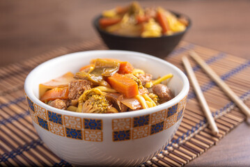 Vegan food, Vegan Yakisoba, with chopsticks in a bowl on bamboo mat, over wood, selective focus.