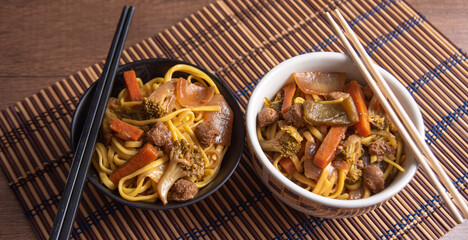 Vegan food, Vegan Yakisoba, with chopsticks in a bowl on bamboo mat, over wood, selective focus.