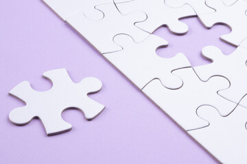 Puzzle pieces on lilac surface. White jigsaw game grid texture. Matching, inserting last missing part. Business and teamwork problem solving background. Copy space for add text, close up.