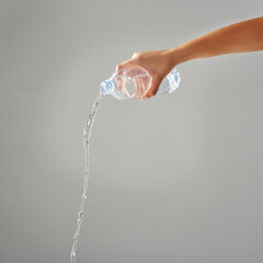 Purified water. Cropped shot of water being poured out of a bottle against a grey background.