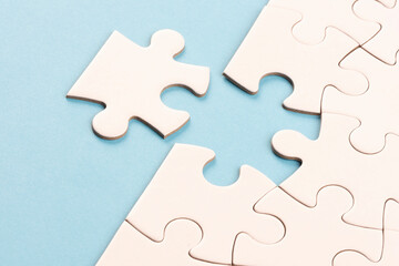 Obraz premium Puzzle edge piece on sky blue surface. White jigsaw game grid texture. Matching, inserting last missing part. Business and teamwork problem solving background. Copy space for add text, close up.