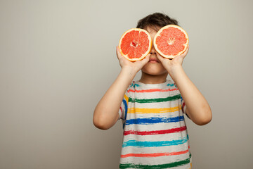 cute boy covers eyes with ruby grapefruit. healthy living concept.