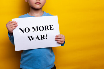 A child in a blue T shirt holds a poster with appeals for peace on a yellow background. no face,...