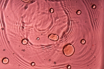 A pattern of pink doses of acid, hyaluronic moisturizing serum or gel on a water background. Abstract backdrop pattern. Cosmetics or healthcare protection concept