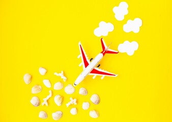 On a yellow background, a model of an airplane approaches sea corals and shells, behind white air clouds.  Space for copy text.  Flat lay.  Buying online tickets.  Booking tours.