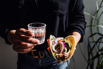 Mexican woman hands holding tacos and mezcal shot traditional food in Mexico city