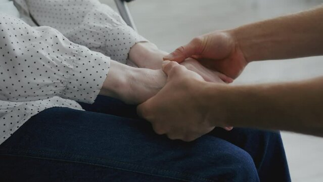 Support group for people with disability. Unrecognizable supporter holding hands of of woman sitting in wheelchair