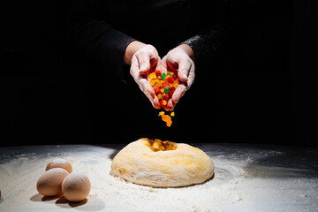 women's hands knead dough with candied fruits for easter cakes. black background