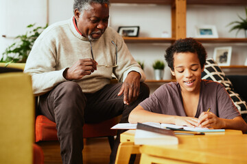 An African-American grandfather is sitting at home with his grandson and helping him with homework.